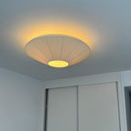 Clérachic pleated ceiling light on a pale ceiling with a warm glow around its rim, above a white sliding wardrobe.
