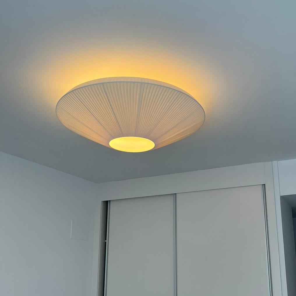 Clérachic pleated ceiling light on a pale ceiling with a warm glow around its rim, above a white sliding wardrobe.