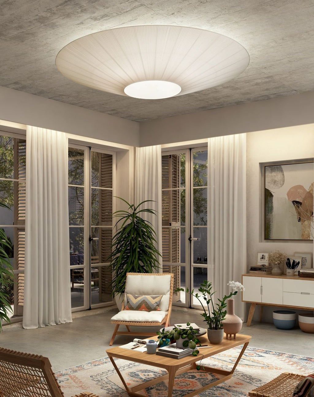 A Clérachic pleated ceiling light in ivory above a living room with French doors, a wooden lounge chair, a coffee table and a tall plant.