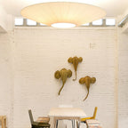 A large Clérachic pleated ceiling light above a white brick wall with three woven animal-head ornaments and a small table below.