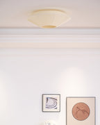 Clérachic pleated ceiling light in cream on a white ceiling with moulded cornice, above two framed prints.