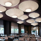Close view of a group of large Clérachic pleated ceiling lights in white, hung from a dark timber ceiling over a conference room.