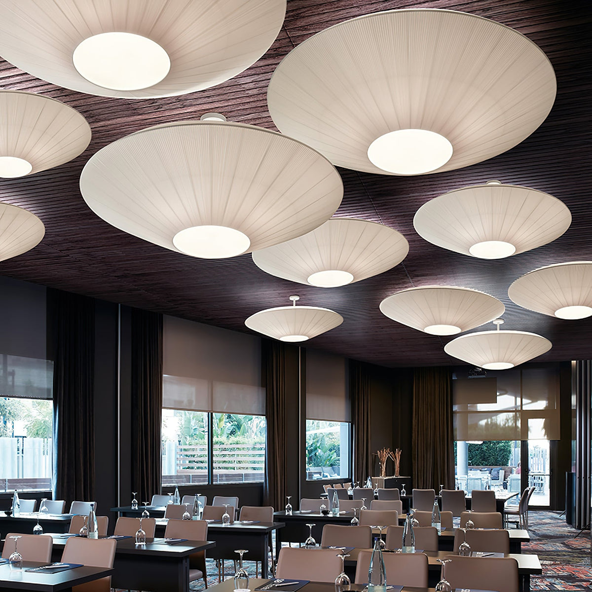 Close view of a group of large Clérachic pleated ceiling lights in white, hung from a dark timber ceiling over a conference room.