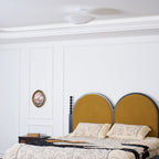 Wider view of a Clérachic white pleated ceiling light above a bed with an arched mustard headboard and floral bedding.