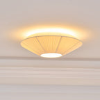 Close view of the lit Clérachic pleated shade, its warm light spilling out around the rim above a moulded cornice.