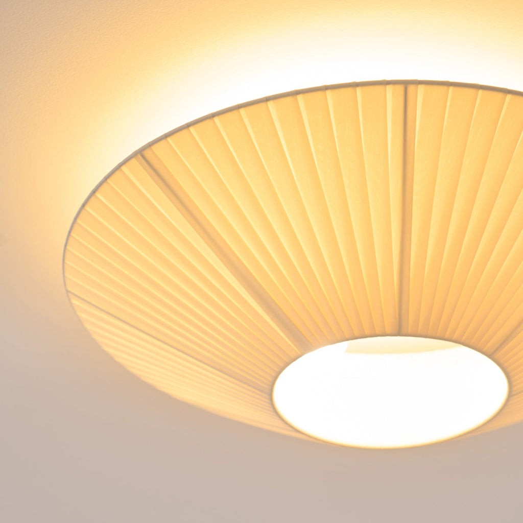 Close view from below of the lit pleated fabric and the round opal diffuser at the centre of this Clérachic ceiling light.