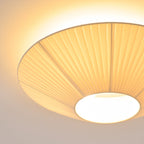 Close view from below of the lit pleated fabric and the round opal diffuser at the centre of this Clérachic ceiling light.