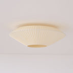 Unlit Clérachic ivory pleated ceiling light seen from the side, with a soft shadow on the pale ceiling above it.