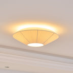 A lit Clérachic pleated ceiling light with seams in its fabric, glowing warm around the rim, above a moulded cornice.