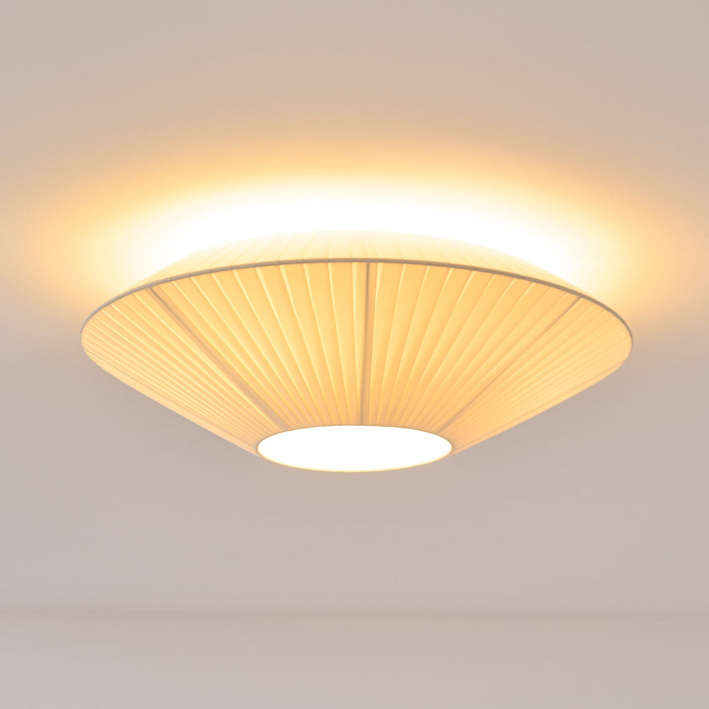 Clérachic pleated ceiling light lit, its pleated shade seen from below with a bright glow around the rim and a white diffuser.