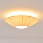 Clérachic pleated ceiling light lit, its pleated shade seen from below with a bright glow around the rim and a white diffuser.