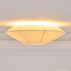 Side view of a lit Clérachic pleated ceiling light, with a wide, flat profile and warm light along the ceiling line.