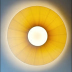 Looking straight up at a lit Clérachic pleated ceiling light, a golden ring of fabric around a white round diffuser.