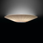 Side view of a lit Clérachic ivory pleated ceiling light with a flat profile, against a dark background.