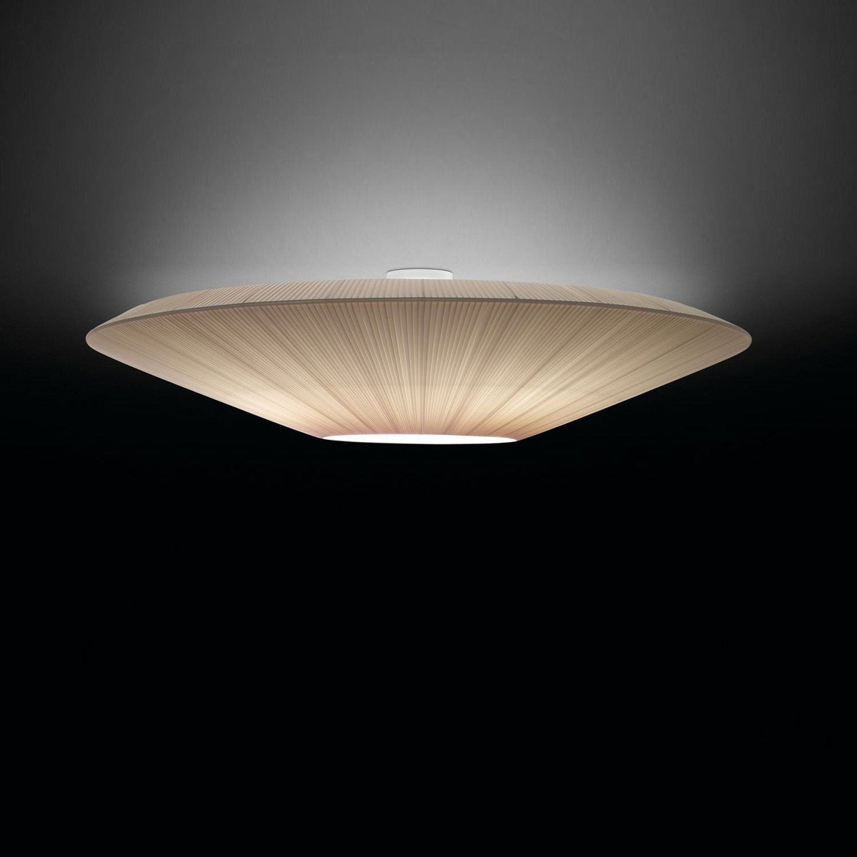 Side view of a lit Clérachic ivory pleated ceiling light with a flat profile, against a dark background.