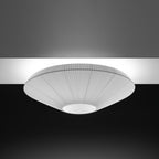 Grey-toned Clérachic pleated ceiling light with a pale opal diffuser, lit against a dark ceiling.