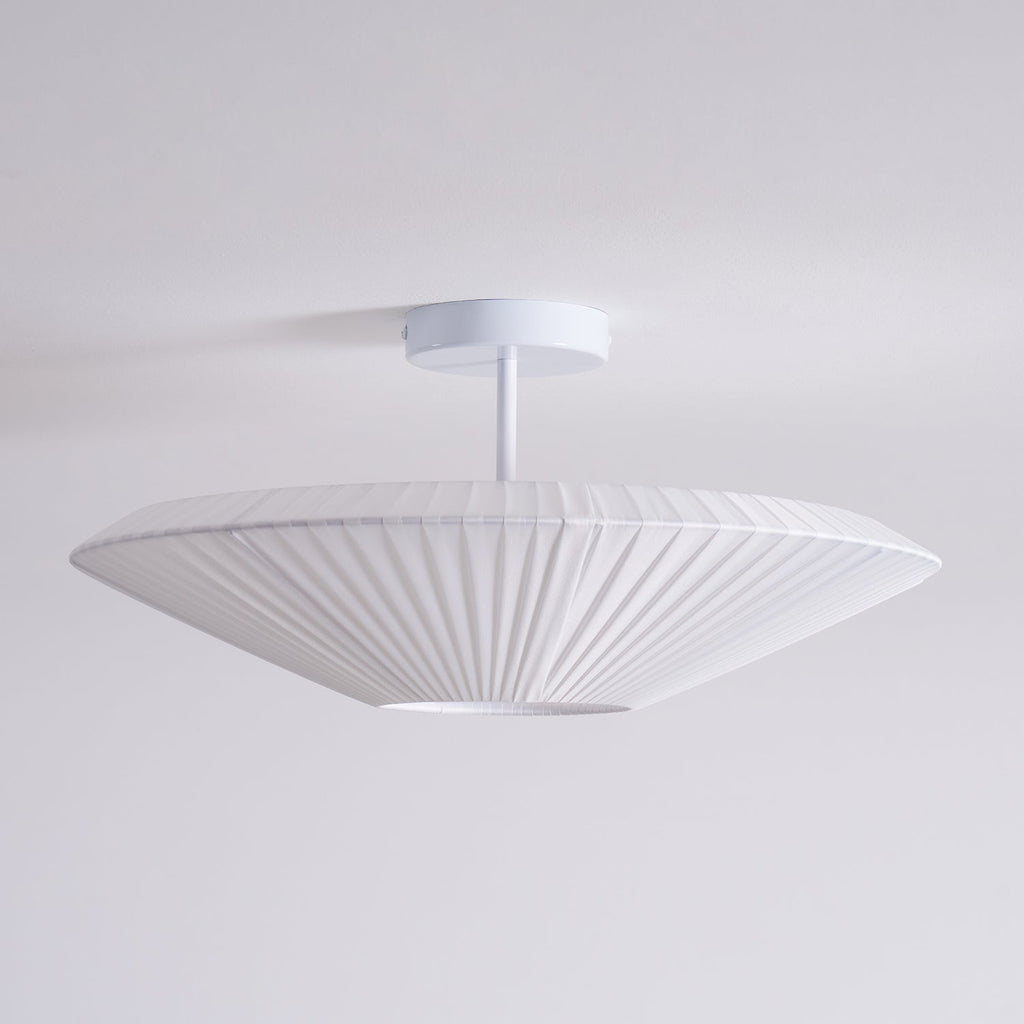 Side view of an unlit Clérachic white pleated ceiling light on a straight stem, with a flat, wide profile against a pale grey wall.