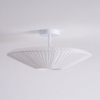 Side view of an unlit Clérachic white pleated ceiling light on a straight stem, with a flat, wide profile against a pale grey wall.