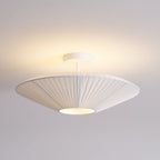 Lit white Clérachic pleated ceiling light with a warm glow on the ceiling above and light shining through the pleats.