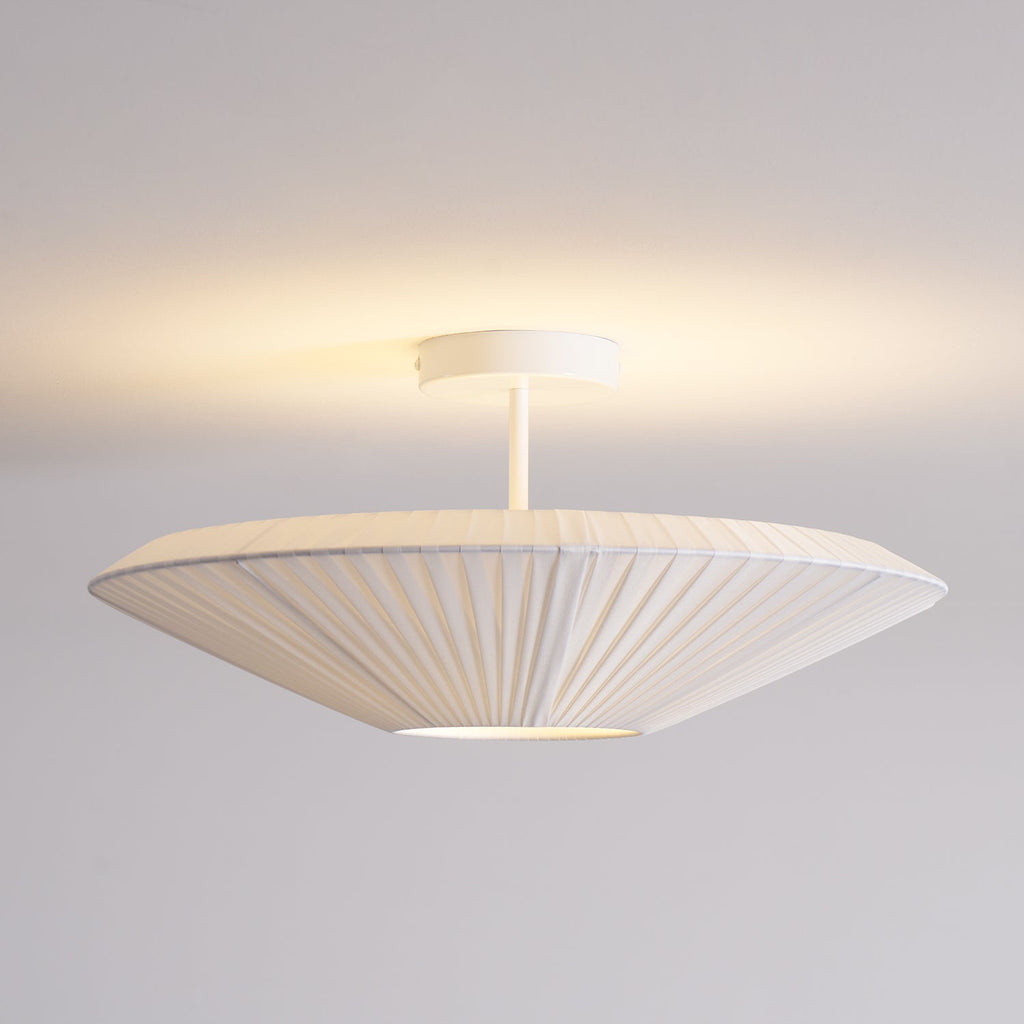 White Clérachic pleated ceiling light on a stem with a round canopy, lit softly, seen from the side against a pale ceiling.
