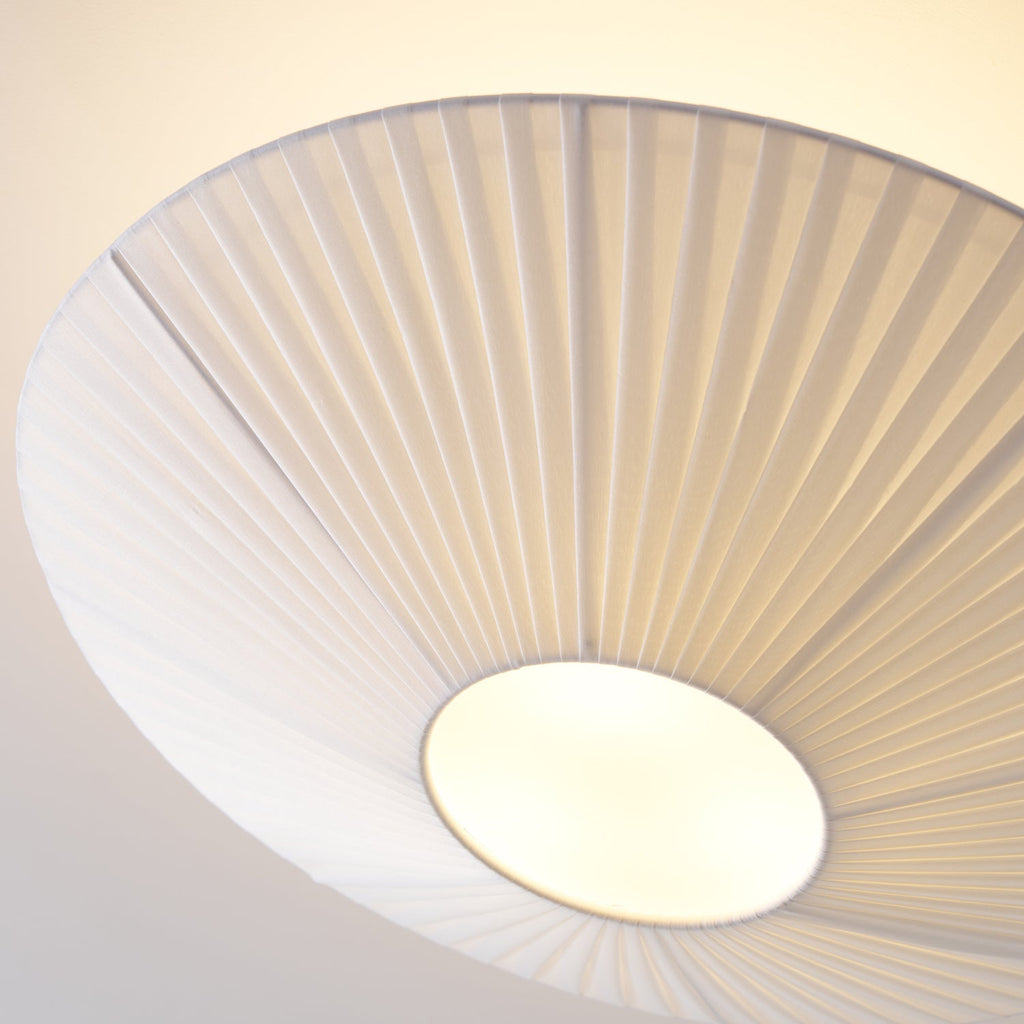 Close view from below of the pleated white fabric and round diffuser on this Clérachic ceiling light, lit warmly.