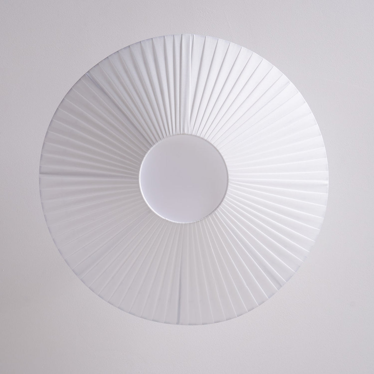 View from directly below at the pleated white shade and the round white diffuser of this Clérachic ceiling light.
