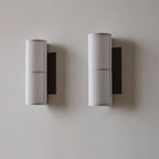 Two white-shaded Clérachic cylinder wall lights side by side on a pale wall, each with a black back plate and a banded fabric shade.