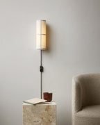 A white Clérachic fabric wall light above a stone side table with a book and a red cup, a boucle armchair at the right.