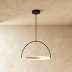 Clérachic black steel pendant with a slim arch hoop holding a pleated white disc that glows softly, hung from a ceiling rod.