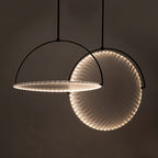 Clérachic two black arch pendants with discs edged in tiny LEDs, one hung flat and one tilted upright, on a dark backdrop.