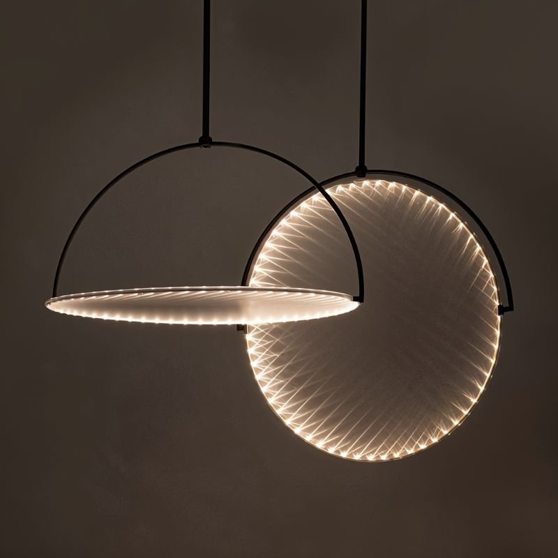 Clérachic two black arch pendants with discs edged in tiny LEDs, one hung flat and one tilted upright, on a dark backdrop.