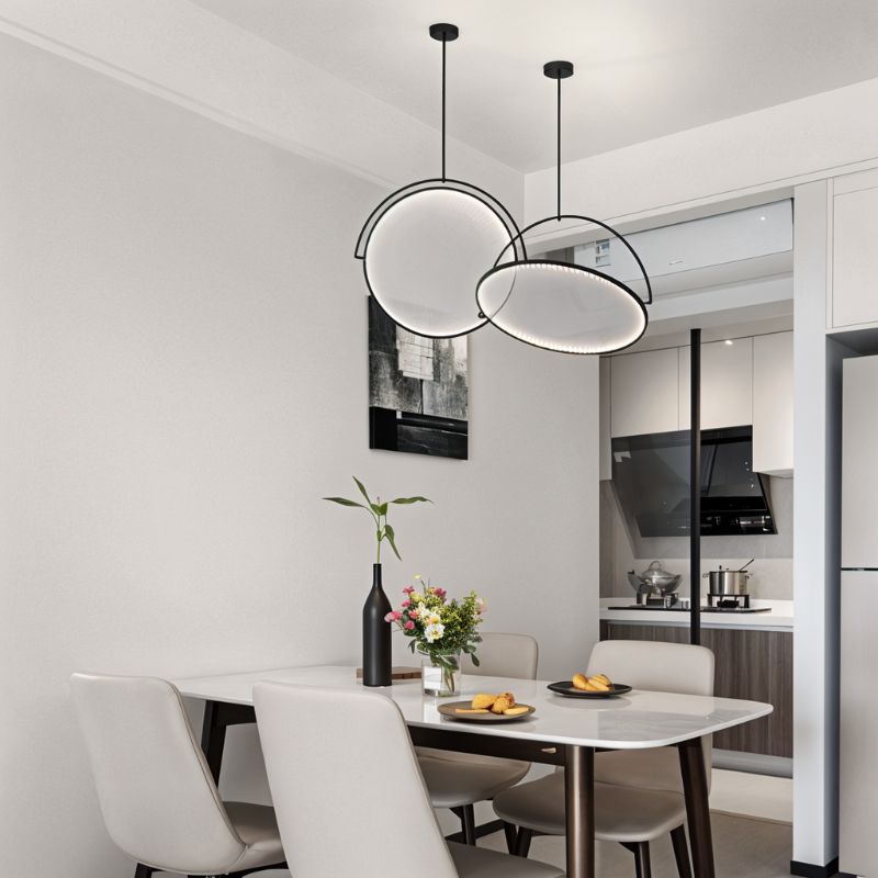 Clérachic pair of black arch pendants with LED-edged white discs hung over a white dining table in an open-plan kitchen.