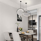 Clérachic pair of black arch pendants with LED-edged white discs hung over a white dining table in an open-plan kitchen.