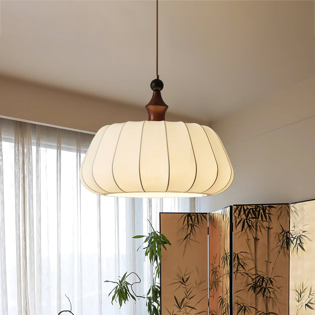 This Clérachic pendant, a ribbed fabric dome with a wood top, hangs by a sheer window and a bamboo-print folding screen.