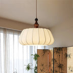 This Clérachic pendant, a ribbed fabric dome with a wood top, hangs by a sheer window and a bamboo-print folding screen.