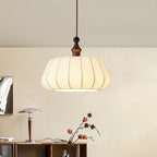 A lit Clérachic fabric dome pendant hangs above a wooden sideboard with a mushroom-shaped table lamp and a branch with orange fruit.
