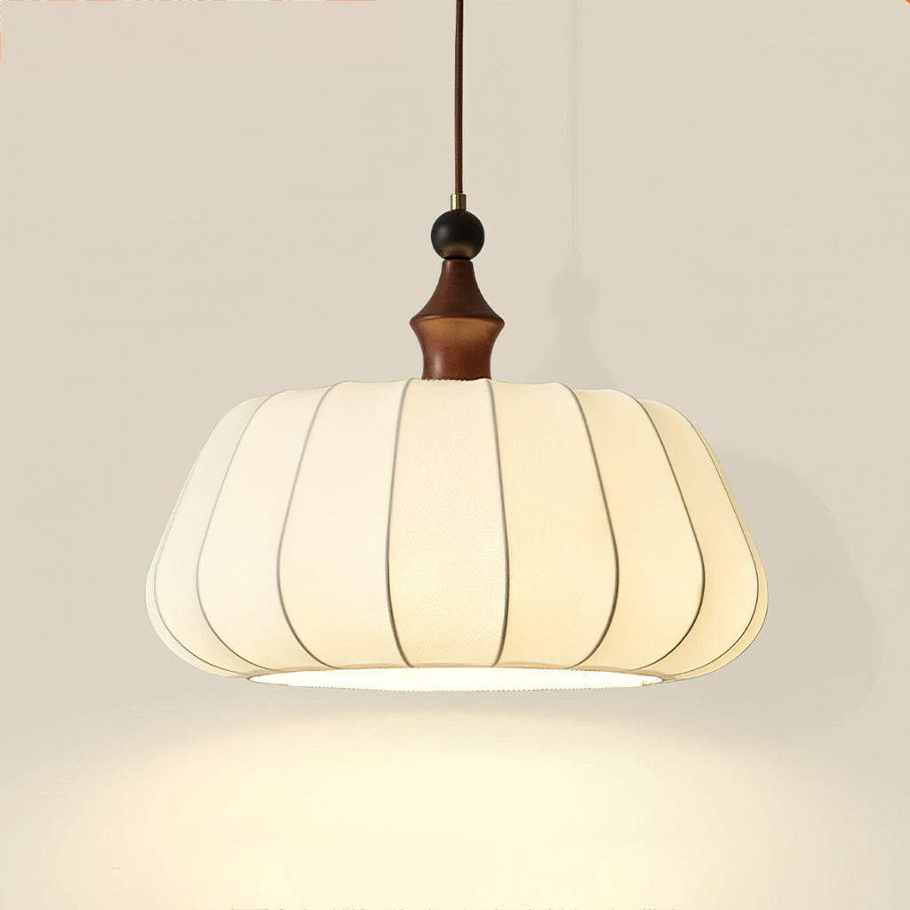Close view of the pleated cream fabric shade, wood top and black bead on this Clérachic pendant, lit warm from below.