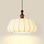 Close view of the pleated cream fabric shade, wood top and black bead on this Clérachic pendant, lit warm from below.