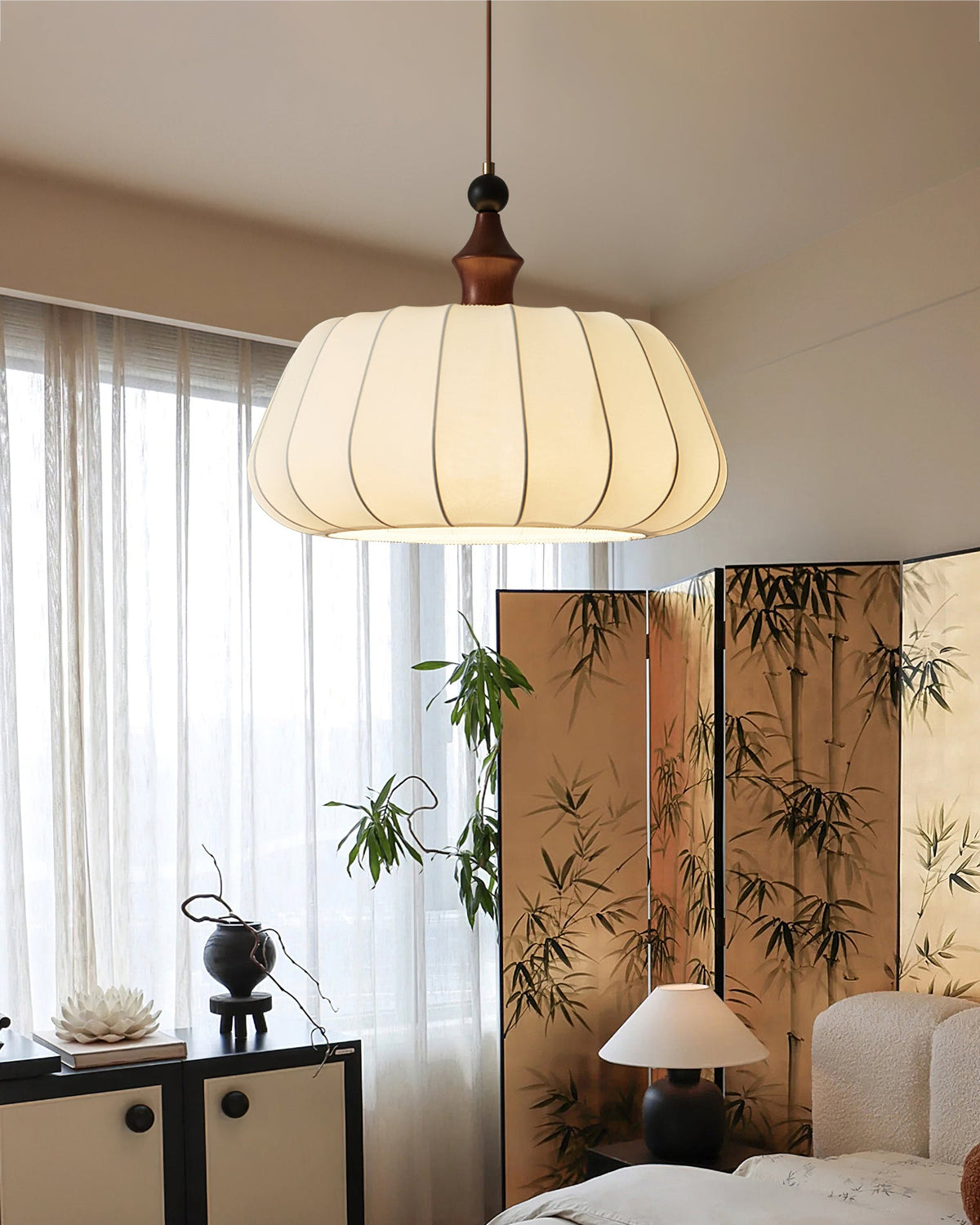 A Clérachic fabric dome pendant hangs by a window with a bamboo-print screen, above a low black cabinet and a cream armchair.