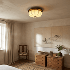 A glowing Clérachic fabric ceiling light in a calm bedroom, with a linen curtain, a landscape scroll on the wall and wooden drawers.
