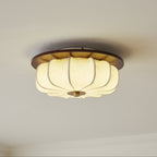 A Clérachic ceiling light with a walnut rim and ribbed fabric shade glows softly against a pale ceiling, seen from below.