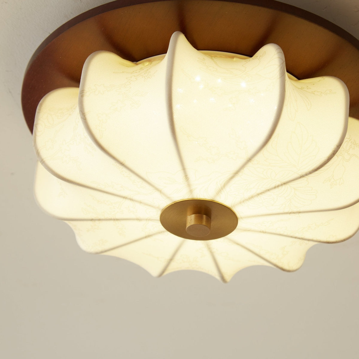 Close view of the ribbed, glowing fabric shade of this Clérachic ceiling light, with a brass centre cap and a walnut rim.