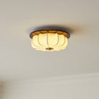 A lit Clérachic fabric ceiling light with a walnut rim and brass cap, above a ceiling cornice, glowing a warm cream.