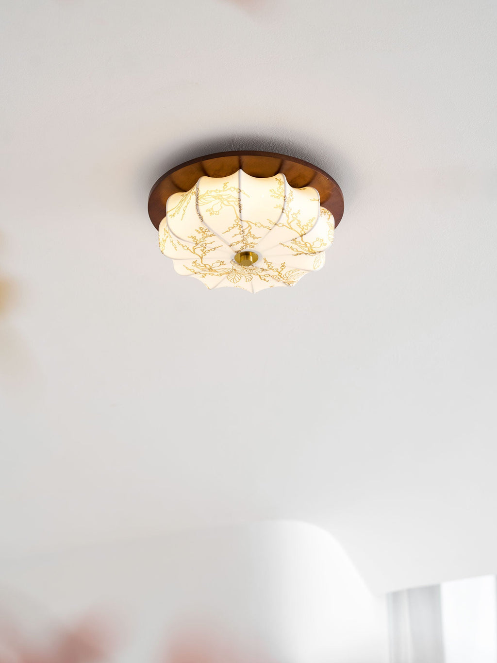 A small lit Clérachic fabric ceiling light with etched floral detail, in a bright white room with sheer curtains.