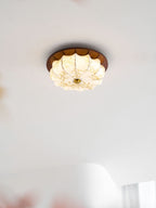 A small lit Clérachic fabric ceiling light with etched floral detail, in a bright white room with sheer curtains.