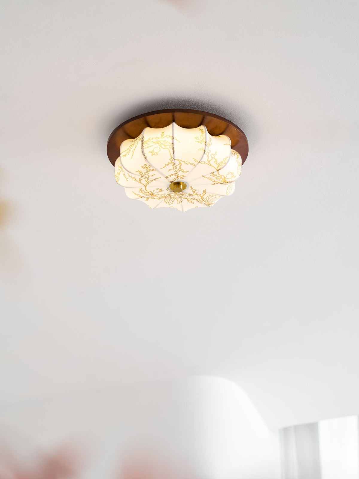 A small lit Clérachic fabric ceiling light with etched floral detail, in a bright white room with sheer curtains.