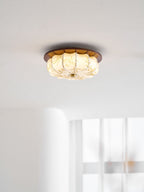 A lit Clérachic ceiling light with a walnut rim and floral-etched fabric shade, near a white wall and sheer curtain.