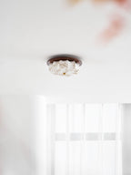 Lit Clérachic ceiling light with a floral-etched fabric shade and walnut rim, seen small above a sheer curtain.