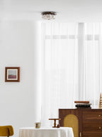 A Clérachic fabric ceiling light seen above a white room, with a walnut sideboard, a small table and a framed print.
