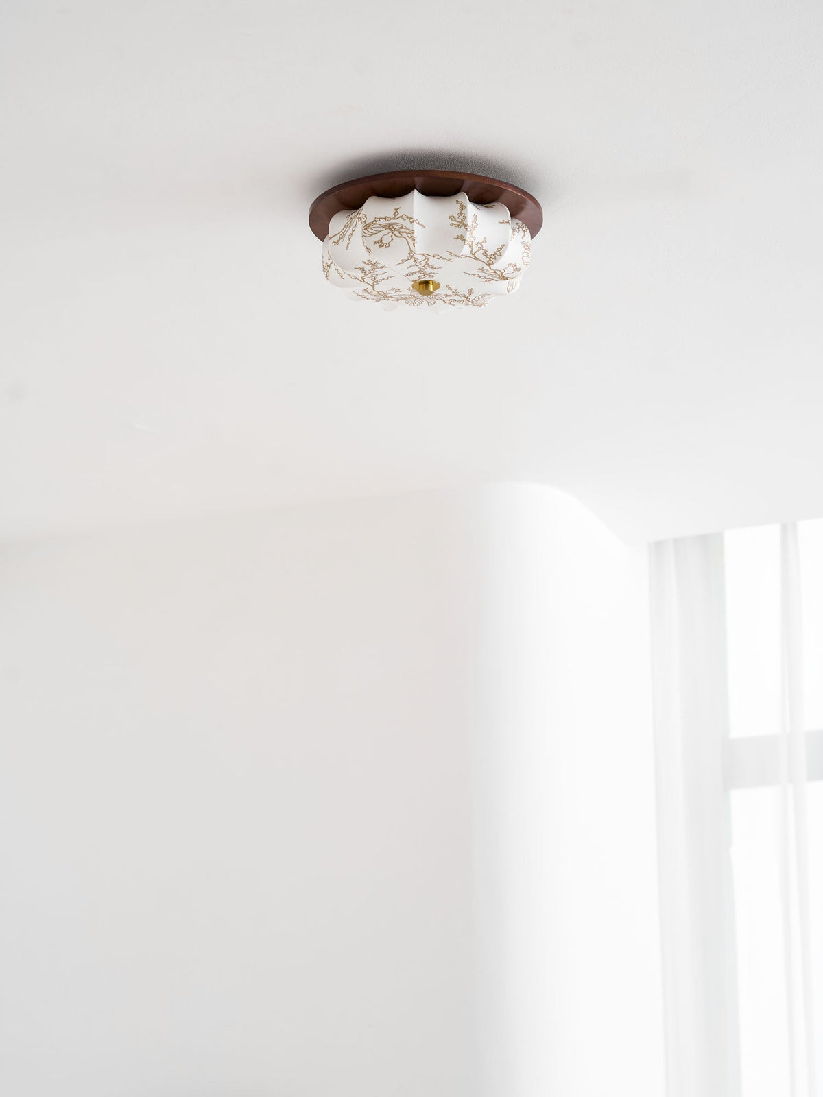A small Clérachic ceiling light with a floral-etched fabric shade and walnut rim, against a white ceiling.